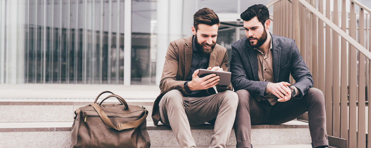 Zwei junge Männer sitzen auf einer Treppe und nutzen Flexible Learning auf einem Tablet